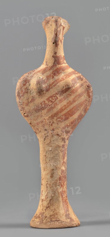 Female idol, unknown Mycenaean workshop, provenance: Königsberg; Frombork Warmian-Masurian Voivodeship — votive offering, female figurine. Female idol in the shape of the letter phi: legs form a cylindrical base widening downward skirt?, arms and torso enclosed in a circle, breasts schematically marked, long cylindrical neck, flat head. Folds of garments, facial features, and eyes simplified using brown paint or varnish; painted surface worn in places. Date: 1400–1200 BC previous dating: 1600–1100 BC. Origin: Mycenae, Greece. Typology: figurine, votive offering. Dimensions: height 12.7 cm; width 4.6 cm; depth 2.8 cm; weight 0.05 kg., A roughly shaped upright clay figure with an elongated neck and flared base, showing a rounded upper body with subtle raised forms where breasts would be, and a narrow tapering lower torso; the surface is textured and worn with patches of reddish-brown paint forming diagonal banding across the upper body and scattered mottled areas elsewhere, and the under...