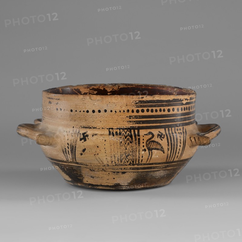 Skyphos mug with depictions of ducks, Skyphos with a profiled belly. Just below the rim are two painted bands with a delicate line. The metopes depict ducks with long necks and legs, in front of which are stylized flowers; one bird is very poorly preserved. Behind each bird's head is a swastika motif. Possibly silhouette technique. Vices placed at the maximum width of the belly. Inner surface covered with matte, faded paint. A reserved line is left a short distance from the bottom; the bottom is undecorated. Technology: Visible traces of turning. Varnish worn away in places. Clay light yellow with many inclusions. Surface shows significant abrasions and chips. Condition: Spout damaged. Visible conservation additions old glue. Clay/color notes: Black: 7.5 YT 2.5/1 black Red: 10 R 4/4 weak red Dated to ca. 725–700 BC Late Geometric period; 9th–8th century BC reference. Origin: Attica. Vessel type: skyphos. Height 9.0 cm; width 19.6 cm; depth 15 cm; weight 0.352 kg., A shallow rounded cer...