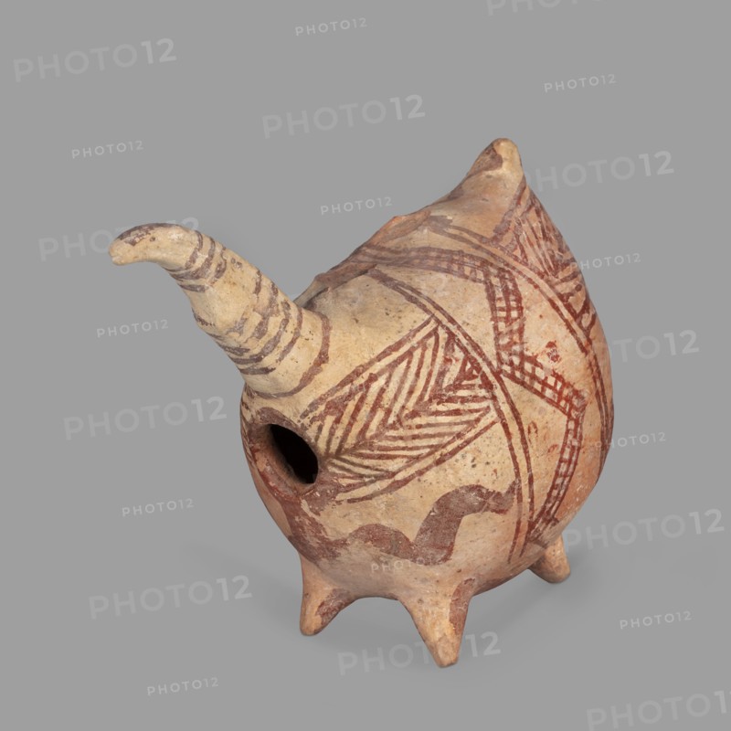 Vessel in the shape of a fantastic animal. The neck is long and thin, ending in a triangular, slightly flattened head. The eyes are marked with depressions; the ears are oblong and flat. Geometric decoration covers the entire surface. At its widest point the body is surrounded by a band consisting of a zigzag band covered with a checkered pattern; from this band herringbone stripes radiate at right angles to front and back. Beneath these are wavy stripes of paint. A series of thin lines on the neck; a hole in the front under the neck. Unknown Cypriot workshop, 1900–1600 BC Late Bronze Age II. Terracotta vessel, height 10.7 cm, width 12.5 cm, depth 6.8 cm., A pottery vessel with a rounded body and a protruding spout, standing on a few short conical legs, with a small circular opening on one side; the surface shows painted linear and geometric patterns including diagonal hatchings and curved bands in reddish-brown on a beige clay background, and the spout bears similar reddish-brown stri...