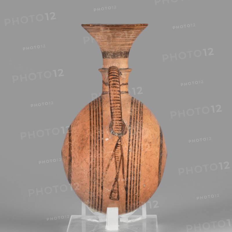 Bottle, geometric motifs, Cypriot pottery, vessels, circles iconography. Amphora with a round, slightly flattened flask-like belly. Brown-black decoration of concentric circles of varying thickness on the belly, horizontal lines on the rim, and a fine zigzag. 1050–750 BC Cypriot-Geometric Period, Cyprus. Vessel, amphoriskos. Height 10.4 cm, width 6.7 cm., A rounded ceramic vessel with a narrow neck and flaring rim sits upright on a clear support against a neutral gray background; the vessel is primarily terracotta orange with dark brown to black painted linear and geometric banding, including several vertical stripes down the body and a patterned vertical handle that connects the rim to the shoulder, and the rim shows concentric horizontal lines and darker worn areas.