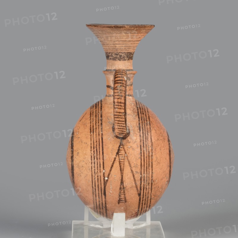 Bottle;, Amphoriskos amphora with a round, slightly flattened flask-like belly. Brown-black decoration of concentric circles of varying thickness on the belly, horizontal lines on the rim, and a fine zigzag. Geometric motifs; circles. Cypriot pottery, 1050–750 BC Cypriot–Geometric Period, Cyprus. Vessel. Height 10.4 cm; width 6.7 cm., An earthenware vessel with a rounded body and a tall flaring neck sits upright on a clear support against a gray background; the vessel is predominantly terracotta orange with dark brown to black painted linear and geometric motifs including vertical stripes and triangular shapes, a single curved handle runs from the neck to the shoulder and is decorated with horizontal dark bands, the neck flares outward with concentric dark lines and a darker band near its base, the surface shows small areas of wear and lighter spots.