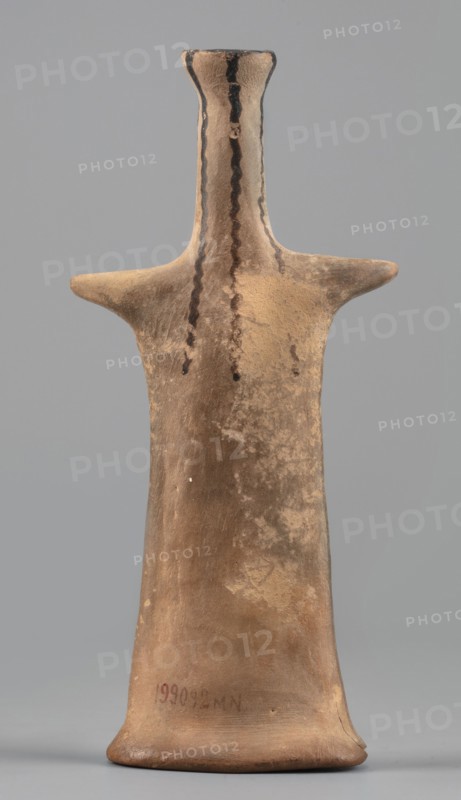 Idol, female idol made of orange clay, votive figurine, 6th century BC 1st half of the 6th century BC, Boeotia; figurine; height 14.4 cm, width 6.7 cm, depth 2.9 cm, weight 0.10 kg., A tapered, humanlike clay figurine in earth tones of brown and tan stands upright against a plain gray background, with a narrow neck and flared top, short horizontal arm-like projections, and wavy dark brown painted lines running down the front of the neck and torso, along with irregular darker and lighter patches across the surface that suggest weathered texture.