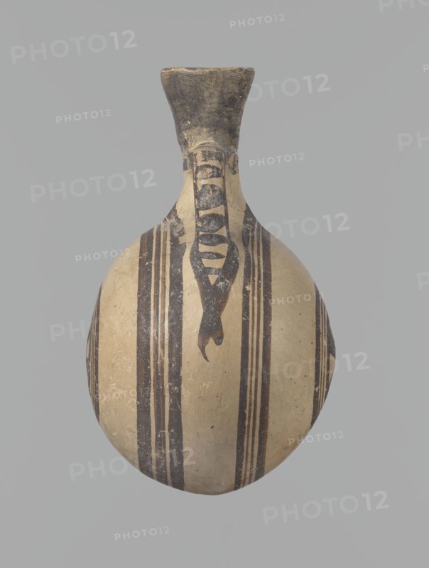 Canteen, Cyprus. Cypriot ceramics, White Painted I . Canteen decorated with concentric circles. Vessel with a spherical, slightly flattened body width on one side 8.5 cm, on the other 7.3 cm, two vertical cylindrical handles and a narrow neck. Slightly flaring spout reconstructed. Pinkish clay with creamy engobe and black-brown decoration. On the handles: horizontal lines framed by thick lines that connect at the neck at the attachment point and intersect below the handles. The two flattened sides of the body are decorated identically with two sets of concentric circles composed of four lines each: two narrow lines framed on both sides by wider lines. The outer line of the outer band overlaps the neck and slightly extends over the handle mounts, widening there. The center of the inner band is filled with a Maltese cross motif. Good condition: reconstructed spout and upper half of the neck. Limescale deposits have been removed. Numerous abrasions, especially on the neck and handle mount...