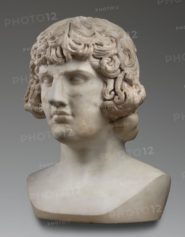 Portrait of Antinous, unknown Roman workshop, male portrait bust, Roman sculpture, 130–138 CE, Roman Empire 27 BC–476, marble sculpture, weight 59.5 kg, height 54 cm, width 40 cm, depth 32 cm, A marble bust of a person shown from the shoulders up with curly, textured hair and a smooth face, rendered in shades of white, off-white, cream, and light beige, set against a neutral gray background; the hair has deeper carved grooves creating shadowed areas that appear slightly darker, and the surface of the bust shows subtle discoloration in warm beige and pale brown tones on the cheeks and neck.