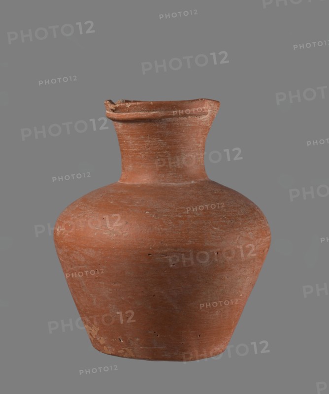 Jug. Jug with a biconical belly, widest at about half its height; broad, not very sloping shoulders; wide neck slightly widening toward the spout, the neck about one-third of the vessel's total height. Spout profiled, irregular, slightly raised and extended on one side forming a small secondary spout; cross-section almost triangular with a ~1 mm indentation at centre of outer profile. Bottom very slightly rounded. Made of Nile clay NB1? according to the Vienna System. Neck was made separately and joined to the body; joint traces erased. Outer surface smoothed, covered with an engobe and polished. Inner surface smoothed except for the neck, which is also engobed and polished. Color reddish-brown. Well preserved with slight chipping at the rim and areas of engobe worn off on the outer surface. Edfu — local workshop. Old Kingdom comparative parallels: Reisner, type XIX–XX, ca. 2686–2181 BC. Measurements referenced in comparative material: example height 17.4 cm; rim Ø 8.1 cm; body Ø 15 cm...