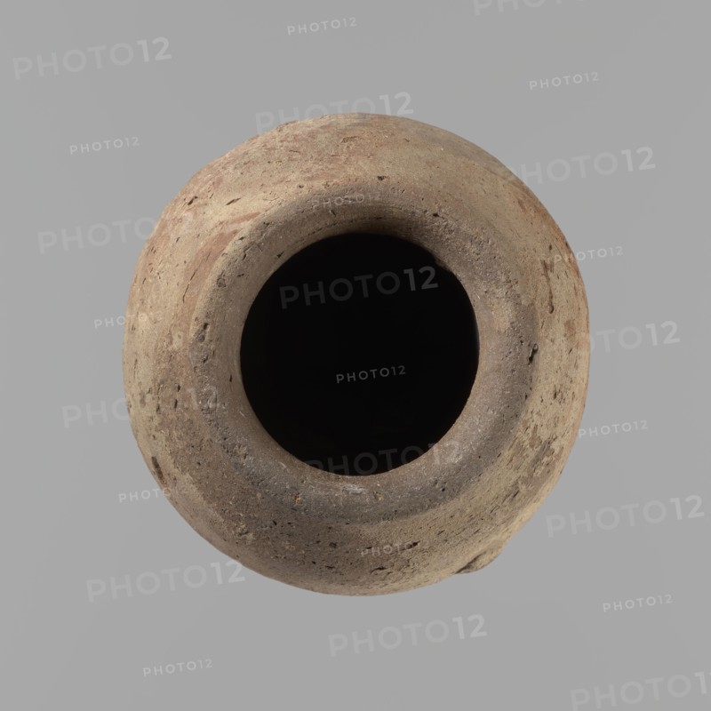 Vessel with hieratic inscription. Conical Nile-clay NB2 vessel, tapering toward a pointed bottom; irregular, widest at approx. 3/4 of the height. Narrow, slightly sloping shoulders; short, wide neck; very gently rounded, slightly flaring rim. Handcrafted, with upper part shoulders, neck, rim turned. Smooth surface, externally probably covered with engobe. Remains of a hieratic inscription in black on the lower belly. Complete, well preserved. Old Kingdom, ca. 2686–ca. 2181 BC; findspot Edfu. Height 12.9 cm; rim diam. 5.5 cm; body diam. 7.8 cm. Comparative parallels: Petrie Dendera, Abydos, Hope Akhmim, Reisner Mycerinus; Naga ed-Der, Brunton Qau and Badari, Mace Naga ed-Der II, Keiser et al., A round, textured clay vessel viewed from above with a wide dark opening at its center; the vessel surface shows rough, uneven textures and small pits and chips, with visible color variations including shades of tan, brown, beige, and hints of reddish-brown, set against a smooth gray background.