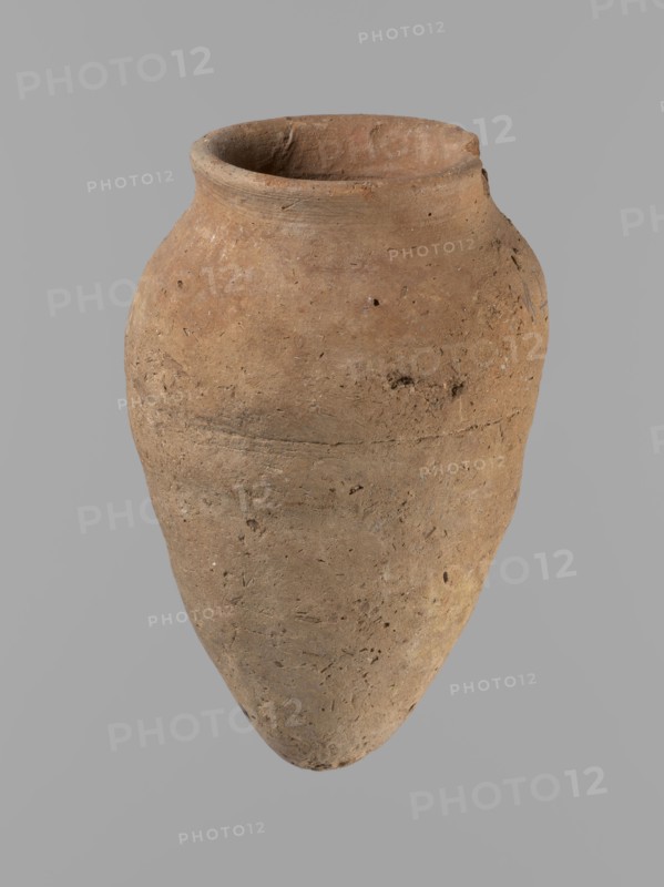 Vessel with hieratic inscription, Egyptian ceramic conical vessel clay, tapering to a pointed bottom, irregular; widest approx. 3/4 of the height. Narrow, only slightly sloping shoulders; short, wide neck; very gently rounded, slightly flaring rim. Handcrafted: upper part shoulders, neck, rim turned. Smooth surface, externally probably covered with engobe. Made of Nile clay NB2 Vienna System. Remains of a hieratic inscription in black oak on lower belly. Complete, well preserved. Old Kingdom, Edfu; height 12.5 cm, rim diameter 5.4 cm, belly diameter 8 cm. Comparative material: Petrie, Dendera pl. XVI.2; Hope, Akhmim fig.7 type AIVa 2bi; Reisner, Mycerinus p.212 fig.64; Brunton, Qau and Badari pl. LXXXI type 77N; Mace, Naga ed-Der II figs.87.11–25; Reisner, Naga ed-Der III figs.28–33; Petrie, Abydos II pl. XLIII; Keiser et al., MDAIK 40 fig.9b — ca. 2686–2181 BC., A single large clay vessel with a rounded shoulder and a tapered base sits against a plain gray background; the pot has an o...