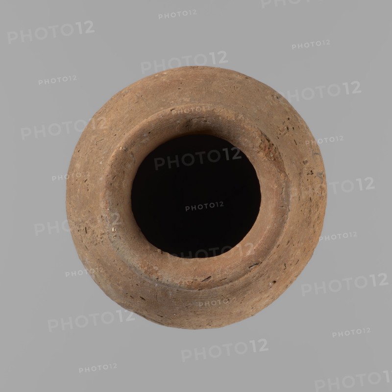 Vessel with hieratic inscription. Egyptian conical clay vessel, tapering toward the bottom, irregular, widest at approx. 3/4 of the height. Narrow, only slightly sloping shoulders; short, wide neck; very gently rounded, slightly flaring rim; pointed bottom. Handcrafted: upper part shoulders, neck, rim turned. Smooth surface, externally probably covered with a layer of engobe. Made of Nile clay NB2 Vienna System. Remains of a hieratic inscription in black in the lower part of the belly. Complete, well preserved. Old Kingdom, ca. 2686–2181 BC. Dimensions: height 12.5 cm; rim dia. 5.4 cm; belly dia. 8 cm. Comparative parallels cited Petrie, Hope, Reisner, Brunton, Mace, Keiser et al.., A round, worn clay vessel viewed from above with a wide dark opening at its center; the vessel surface shows a rough, textured appearance with small pits and specks and a warm brown to reddish-brown color against a solid light gray background.