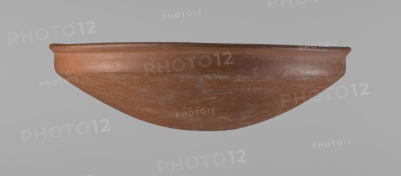 Medum-type bowl, Egyptian ceramics, Medum-type bowl with characteristic carination under the rim. Rounded bottom. Straight rim, slightly flaring. Narrow, very sloping shoulders—almost vertical. The diameter of the rim is larger than the diameter of the shoulders of the vessel. Clay probably NB. The surface of the vessel is leveled and covered with a layer of engobe, then polished. Vessel color: red. Vessel complete, very well preserved. Comparative material: Junker, Giza I, pl. I,2,16, c. 2686–c. 2181 BC; Old Kingdom late Old Kingdom. Provenance: Edfu. Vessel height 7.5 cm; diameter rim 25.8 cm; diameter shoulders 25.2 cm., A shallow, rounded bowl with a wide rim is shown against a plain gray background; the bowl has an overall reddish-brown terracotta color with areas of lighter brown and faint grayish-white discoloration, a slightly rough surface texture with visible scuffs and small pits, a gently curved profile tapering to a rounded base, and the rim appears slightly thicker and sm...