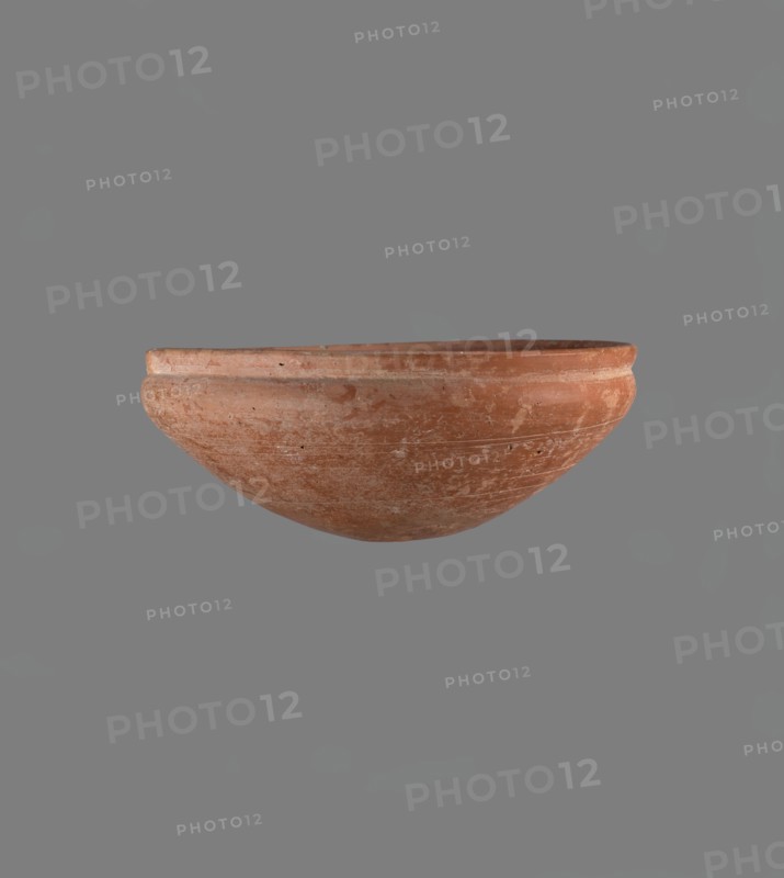 Medum type bowl. Medum type bowl with characteristic carination under the rim. Rounded bottom. Straight rim, slightly flaring. Narrow, sloping shoulders. The diameter of the rim is smaller than the diameter of the vessel's shoulders. Clay probably NB1. Surface leveled and covered with a layer of engobe, then polished. Vessel color - red. Complete vessel, very well preserved. c. 2686–c. 2181 BC; Old Kingdom, Edfu. Vessel, height 4.2 cm, diameter 21.1 cm rim, diameter 21.1 cm shoulders., A single shallow, rounded clay bowl with a slightly raised rim sits centrally against a plain background; the bowl shows a weathered surface with scratches, patches of lighter wear, and small pits, and the visible colors include terracotta, light brown, pale beige, and hints of gray.