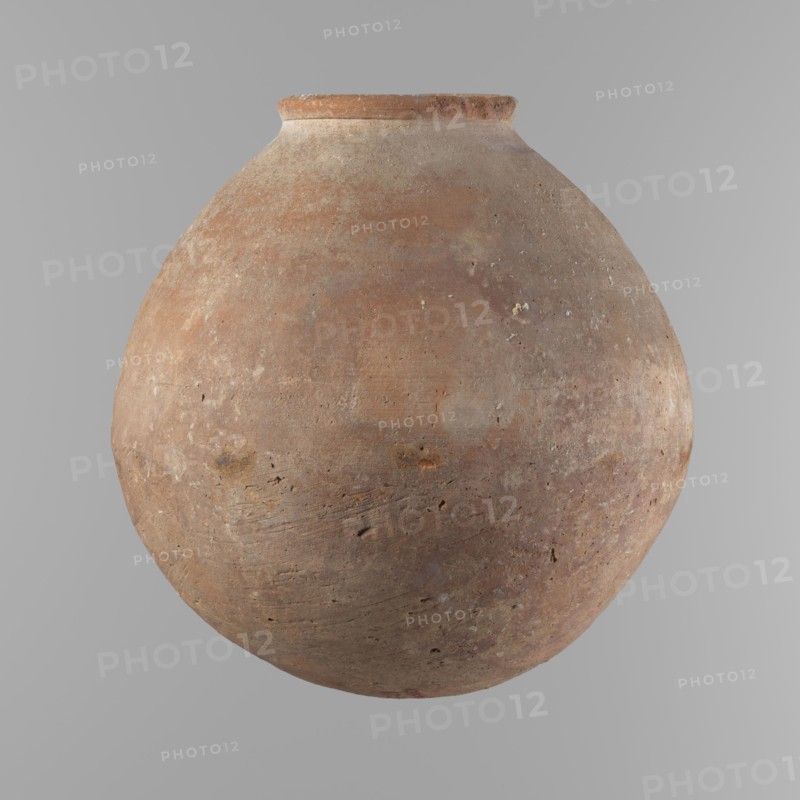 Vessel with an almost spherical belly, widest about 1/3 of the vessel's height. Sloping shoulders. Neck poorly defined – very short and wide. Rounded, slightly flaring rim. Rounded bottom. Made of Nile clay NB. Surface smooth; outer surface finished to about half its height with a knife or similar tool. A rather indistinct cord impression around the widest diameter of the belly. Light red color. Chipped rim and traces of salting in places over the entire surface. Comparative material: Reisner, Mycerinus, fig. 62.3 type II, III, ca. 2686–2181 BC; Old Kingdom, Edfu, vessel, height 24.9 cm, diameter 10.3 cm rim, diameter 24.2 cm body., A large rounded clay vessel with a narrow rim, showing a weathered, textured surface in shades of brown, reddish-brown, tan, and gray, with small pits, scratches, and uneven patches across its curved body, set against a smooth light gray background.