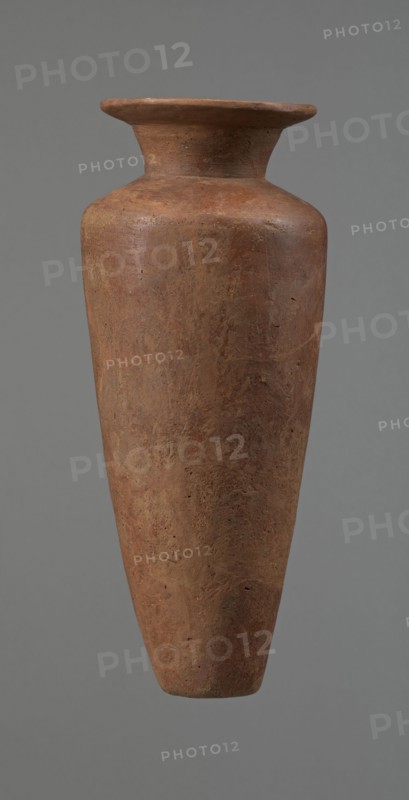 Vessel, Egyptian pottery, Type HS vessel of conical, slender shape, widest at about 3/4 of the height. Shoulders wide, almost horizontal, slightly sloping. Neck wide, short, funnel-shaped in its lower part, widening towards the rim from about half its height. Rim wide, flat in the upper part, slightly rounded at the bottom, slightly asymmetrical. Bottom flat, slightly asymmetrical. Neck made separately and attached to the shoulders. Surface even. Lower part finished to approximately 3/4 of its height using a knife or similar tool. Outer surface and inner surface of the rim and neck covered with a layer of dark red engobe and polished. Color dark red. Vessel reconstructed from many original fragments; gaps filled with plaster. c. 2686–c. 2181 BC Old Kingdom, Edfu. Vessel; height 24.8 cm, rim diameter 8.9 cm, shoulder diameter 10.3 cm, bottom diameter 4.1 cm., A tall, narrow clay vessel with a flared rim and a slightly tapered neck leading to a rounded shoulder and a long, conical body; ...