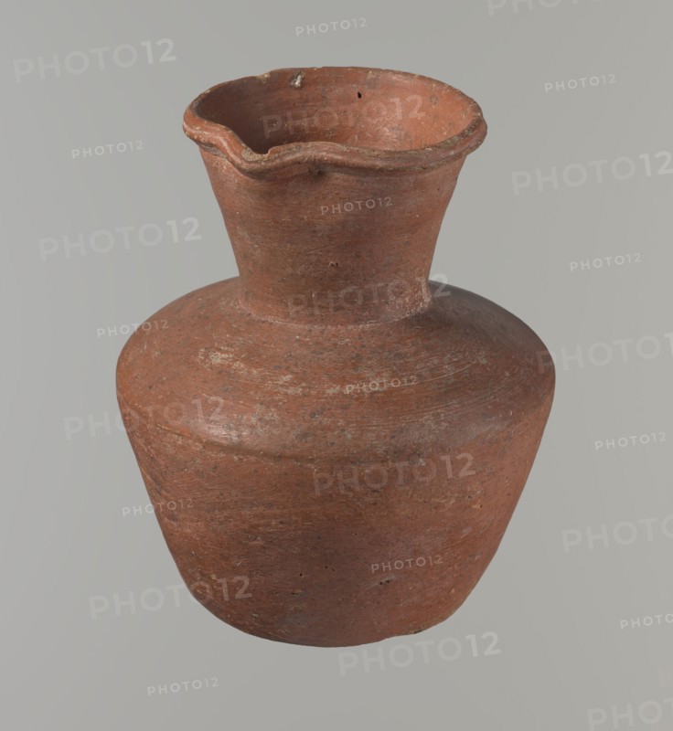 Vessel, Egyptian ceramics, clay vessel, jug. Medium-sized jug with a biconical body, widest at about half its height. Wide shoulders, not very sloping. Wide, almost cylindrical neck widening towards the spout; neck height about one-third of total vessel height. Profiled, irregular spout, slightly raised and extended on one side forming a small spout. Spout nearly triangular in cross-section, with an approximately millimeter-sized cylindrical bulge at center of outer profile. Bottom almost flat with very slight rounding. Made of Nile clay NB1? — Vienna System. Neck possibly made separately and attached to the shoulders. Outer surface smoothed, covered with an engobe and polished. Inner surface smoothed, except for the neck which is also engobed and polished. Color reddish-brown. Fairly well preserved; rim slightly chipped in two places and outer engobe worn in places. Comparative material: Rzeuska, Saqqara II, cat.210–211 form 35; Louvre E 16586. Date: c. 2345–c. 2181 BC; Old Kingdom, 6...