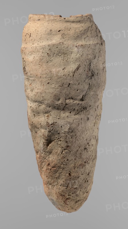 Vessel, Egyptian pottery, hand-made clay vessel with a conical belly, widest in its upper part approximately 4/5 of the vessel's height, rounded bottom. Shoulders irregularly marked—clearly sloping on one side and short, almost horizontal on the opposite. Straight, slightly tapering rim. Made of not very well-worked Nile clay with numerous organic inclusions and limestone particles visible on the surface. Surface uneven and carelessly made, with numerous uneven depressions; cracks on the surface result from poor clay kneading. Brown color. Ca. 2686–ca. 2181 BC Old Kingdom, from Edfu. Vessel; height 38 cm; rim diameter 11.7 cm; body diameter 15.7 cm., An upright, elongated rough-textured object resembling a weathered vessel with an irregular, tapered shape, showing a pitted and cracked surface with varied coarse grain; the surface displays a range of earthy tones including beige, tan, light brown, and hints of reddish-brown and gray, with small darker flecks and spots scattered across i...