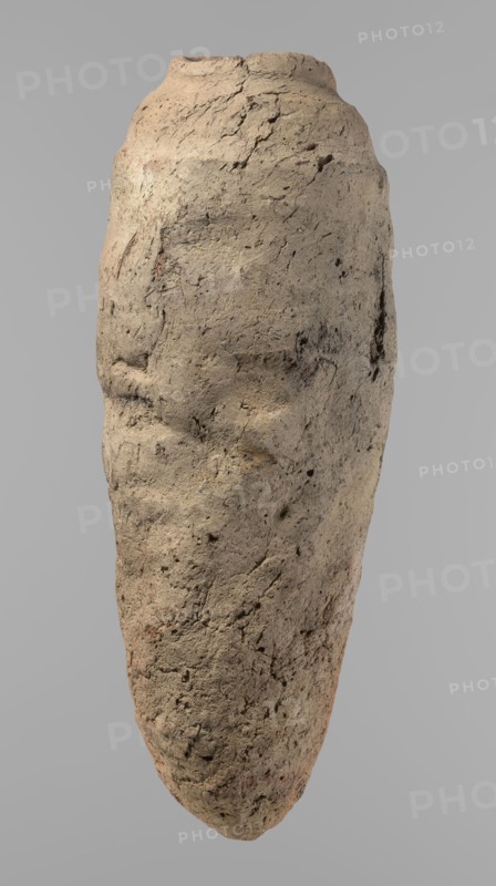 Vessel, Egyptian pottery vessel with a conical belly widest in its upper part approx. 4/5 of the height. Rounded bottom. Irregularly marked shoulders—clearly sloping on one side, short and almost horizontal on the opposite. Straight, slightly tapering rim. Hand-made of not well-worked Nile clay with numerous organic inclusions and limestone particles visible on the surface. Uneven, brown surface with numerous depressions and cracks resulting from poor clay kneading. Ca. 2686–2181 BC Old Kingdom, from Edfu; height 38 cm, diameter 11.7 cm rim, diameter 15.7 cm body., A roughly elongated, irregularly shaped object resembling a weathered stone or clay form fills the image against a plain light gray background; its surface is textured with cracks, pits, and rough patches, showing uneven contours and faint depressions that suggest subtle facial-like features, with a rounded top tapering to a narrower bottom. The visible colors are mainly beige and tan with areas of light brown and small hint...