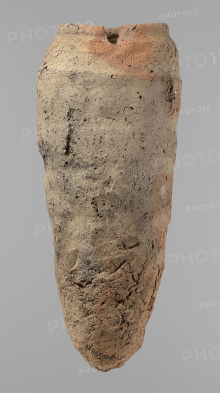 Vessel, Egyptian pottery, hand-made clay vessel with a conical belly widest in its upper part approximately 4/5 of the vessel's height. Rounded bottom. Irregularly marked shoulders—clearly sloping on one side and short, almost horizontal on the opposite. Straight, slightly tapering rim. Made of Nile clay with numerous organic inclusions and limestone particles visible on the surface. Uneven surface with numerous depressions; brown color. Quite well preserved; surface cracks resulting from poor clay kneading. Ca. 2686–2181 BC Old Kingdom, from Edfu. Vessel; height 38 cm, rim diameter 11.7 cm, body diameter 15.7 cm., An elongated, irregularly textured object with a rough, cracked surface in shades of beige, tan, light brown, and areas of reddish-orange, set against a plain gray background; the surface shows small pits, grooves, and rough patches with subtle darker speckles and variations, and the top edge is uneven with a small notch while the overall form tapers toward a rounded point a...