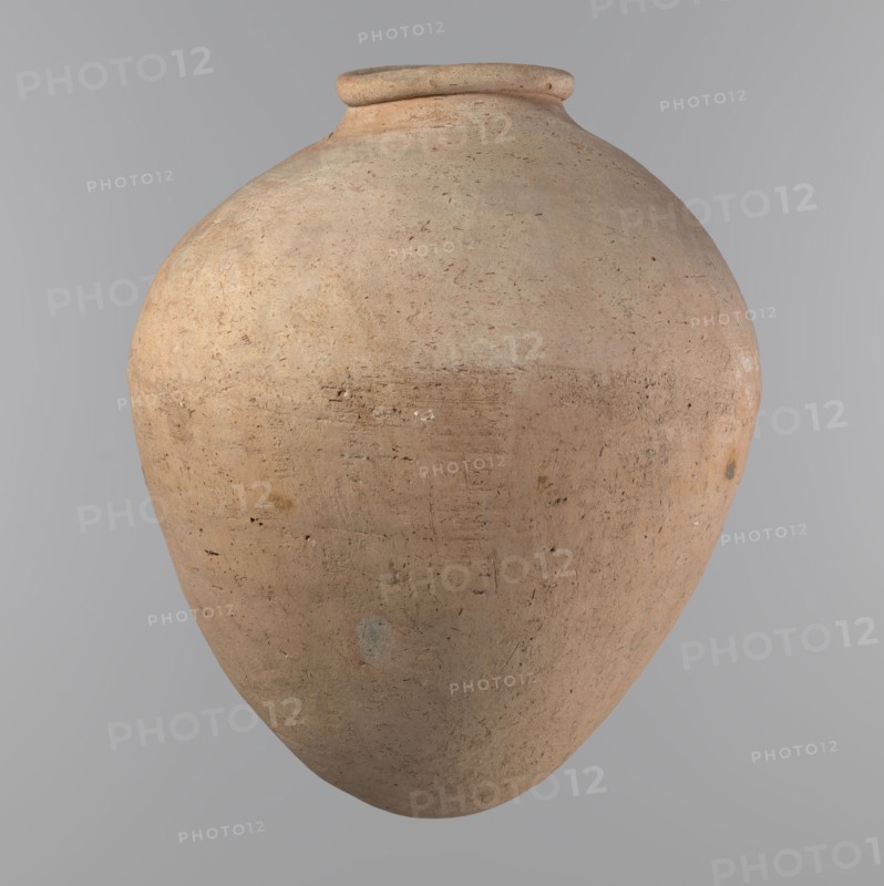 Vessel, unknown author. Egyptian pottery vessel of ovoid, slightly downward-stretched shape, widest at about 2/3 of the height. Broad, sloping shoulders, very short, wide neck. Roller-shaped rim, oval in cross-section, slightly flaring. Rounded bottom. Clay NB2 according to the Viennese System with significant organic admixture. Hand-made from two parts and joined at about 2/3 of the height; upper part turned. Surface leveled, possibly covered with a layer of engobe; traces of a white substance in places on the outer surface and on the rim. Beige color. Well-preserved. Ca. 2686–2181 BC; Old Kingdom, Edfu. Vessel. Height 34.6 cm; rim diameter 11.6 cm; body diameter 29 cm., A large rounded clay vessel with a narrow rim and bulbous body sits against a neutral background; the vessel shows a rough, textured surface with uneven patches and small pits and scratches. The colors visible are tan, beige, light brown, and hints of gray with slightly darker speckles and faint orangey-brown variatio...