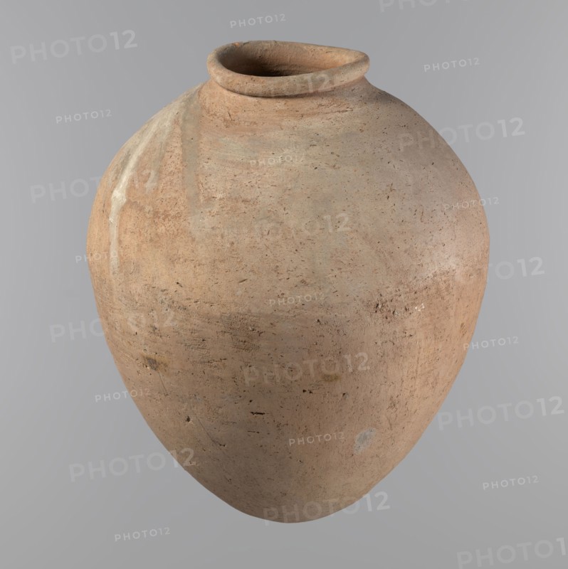 Vessel, Egyptian pottery, ceramic clay vessel of an ovoid, slightly downward-stretched shape, widest at about 2/3 of the height. Broad, sloping shoulders, very short wide neck. Roller-shaped rim, oval in cross-section, slightly flaring. Rounded bottom. NB2 clay Viennese System with a significant amount of organic admixture. Hand-made from two parts and joined at about 2/3 of the height; turned in the upper part. Surface leveled possibly covered with a layer of engobe. Traces of a white substance in places on the outer surface of the body and on the rim. Vessel color beige. Well-preserved. ca. 2686–ca. 2181 BC; Old Kingdom, Edfu; vessel; height 34.6 cm; diameter 11.6 cm rim, 29 cm body., A large rounded clay vessel with an open circular mouth and a turned rim, shown against a plain light gray background; the pot has a textured surface with an earthy palette of tan, light brown, beige, and subtle pale gray patches, with areas of darker brown speckles and occasional small darker spots, an...