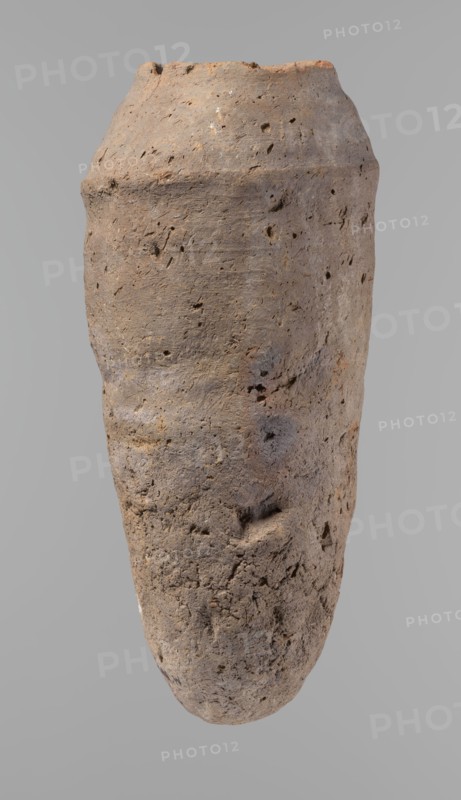 Vessel, Old Kingdom, c. 2686–c. 2181 BC; Edfu; hand-made clay vessel ceramic, height 33.5 cm, rim diameter 10.4 cm, body diameter 15.1 cm., A single tall, narrow, roughly cylindrical object with an irregular, pitted surface and an uneven rim, shown against a plain light gray background; the object displays a range of earthy browns, muted grays, and small areas of rusty orange, with visible texture including small holes, indentations, and rough patches across its surface.