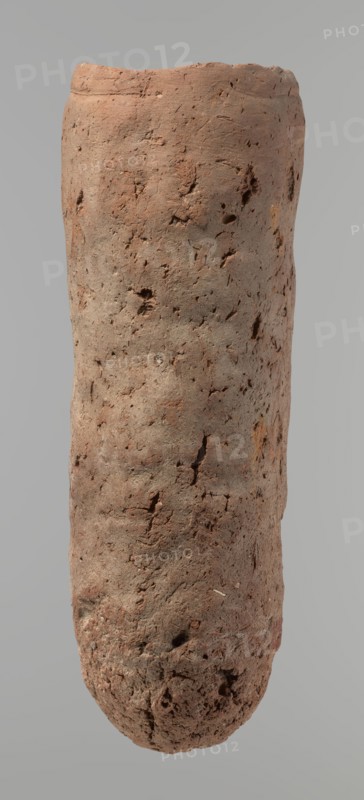 Vessel, Egyptian pottery, hand-made clay vessel. An almost cylindrical vessel, widest in its upper part just below a straight, slightly tapering rim; rounded bottom; shoulders almost illegible. Handmade of Nile clay with numerous organic inclusions and limestone particles visible on the surface; carelessly made with uneven depressions, especially at the bottom; brown in color; cracks on the surface attributed to craftsmanship, kneading and firing. Old Kingdom, ca. 2686–2181 BC; Edfu. Vessel; height 37.9 cm; diameter 11.4 cm rim, 12.5 cm body., A tall cylindrical object with an uneven, rough surface showing a group of small pits and cracks, colored mostly reddish-brown with areas of grayish-brown and hints of darker brown; the top edge is slightly irregular and the bottom is rounded and more textured, with varying surface shadows against a pale gray background.