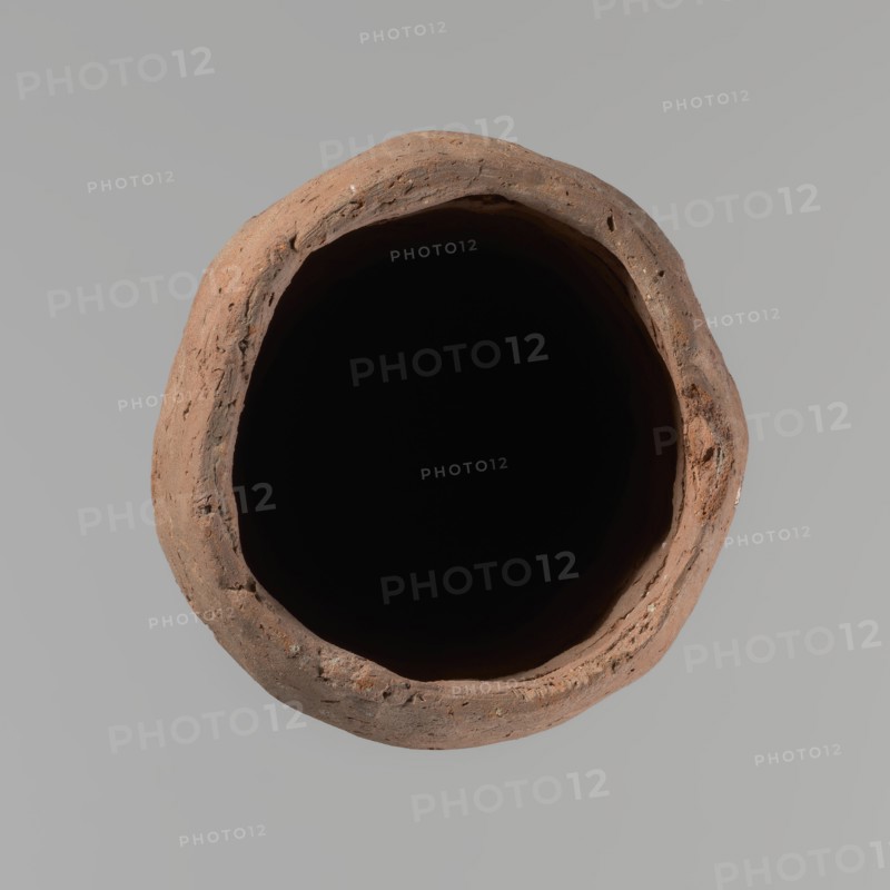 Vessel, Egyptian pottery vessel, clay, hand-made; almost cylindrical, widest just below a straight, slightly tapering rim; rounded bottom; shoulders almost illegible. Handmade of Nile clay with numerous organic inclusions and limestone particles visible on the surface; carelessly made with uneven depressions, especially at the bottom; brown color; cracks on the surface resulting from workmanship and firing. Old Kingdom, ca. 2686–ca. 2181 BC; from Edfu. Height 37.9 cm; diameter 11.4 cm rim, 12.5 cm body., A top-down view of a round, hollow clay vessel with a rough, uneven rim in shades of brown and terracotta surrounding a deep black interior, set against a smooth light gray background.