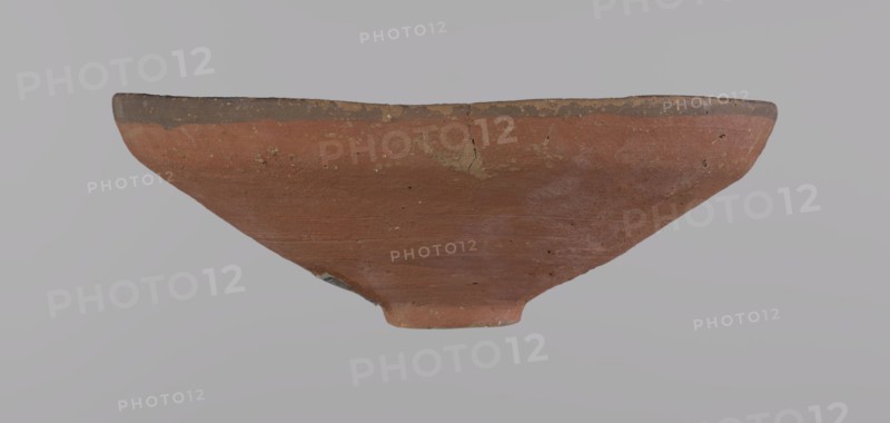 Bowl, Bowl with a conical shape and a ring-shaped foot. Straight rim, slightly flaring outward, irregular. Vessel made entirely on the wheel of Nile clay type ND Vienna System. Surface even, covered with glaze before firing. On the inner and outer surfaces of the rim there is a narrow approx. 0.5 cm black band of decoration. The remainder of the vessel is red. Traces of polish on the surface. The glaze is slightly worn in places—possible traces of use. Good condition—minor clay chips on the rim, abrasions over the entire surface. Analogies: Egypt's Golden Age no. 51, p. 78, ca. 1550–ca. 1425 BC; New Kingdom, early 18th Dynasty. Possible findplaces: Edfu, Deir el-Medina. Vessel; height 5.3 cm; diameter 15.1 cm rim; diameter 3.1 cm bottom., A shallow, wide bowl viewed from the side with a rounded rim and tapered base, showing a weathered surface in shades of reddish-brown and dark brown along the rim, with small areas of lighter beige and gray wear, subtle horizontal striations on the ex...