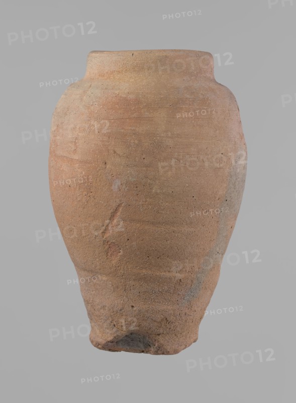 Vessel, Beer jug of a slightly irregular, conical shape with a wide, very short neck and a flat bottom. Flat, narrow shoulders and a gently rounded, straight rim. Wheel-made of Nile clay type NB2 Vienna System. Bottom is cut off with string and bears clear potter's fingerprints, flaring slightly in its lowest part. Surface even; color red. Complete and fairly well preserved, with minor damage to the bottom. New Kingdom, ca. 1550–1069 BC; Edfu. Dimensions: height 24 cm; rim dia. 10 cm; body dia. 16 cm; bottom dia. 9.2 cm., A large rounded clay vessel with a narrow flattened rim and a tapered base, showing an uneven textured surface with small pits and abrasions; the vessel displays a range of earthy colors including terracotta, light brown, pale orange, and hints of gray, with subtle horizontal striations and a few rough patches and marks.