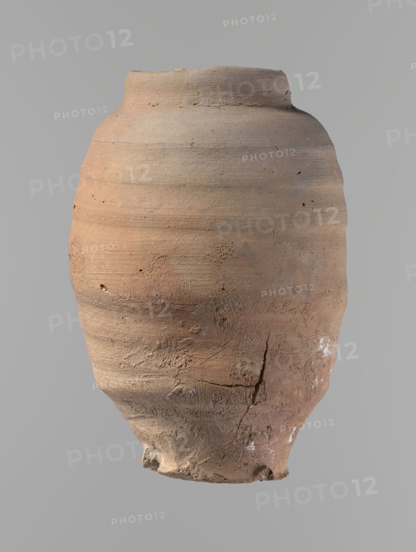 Vessel, Beer jug of a slightly irregular, conical shape with a wide, very short neck and a flat bottom. Flat, straight rim. Wheel-made from Nile clay of type NB2-ND Vienna System. Bottom is cut off with string, with clear potter's fingerprints around the bottom. Surface even. Clay color: red. Vessel complete, fairly well preserved, with minor damage to the rim and small chips on the surface. ca. 1550–ca. 1069 BC; New Kingdom, Edfu. Vessel. Height 24.4 cm; rim diameter 9.8 cm; body diameter 16.3 cm; bottom diameter 8.5 cm., A weathered clay vessel with an uneven rounded body and a narrow rim, showing a rough, textured surface with visible horizontal turning marks and small pits; the lower part has cracks, chips, and areas of abrasion, and there are traces of whitish deposits in places. The visible colors are various shades of tan, brown, reddish-brown, pale beige, and small hints of gray.