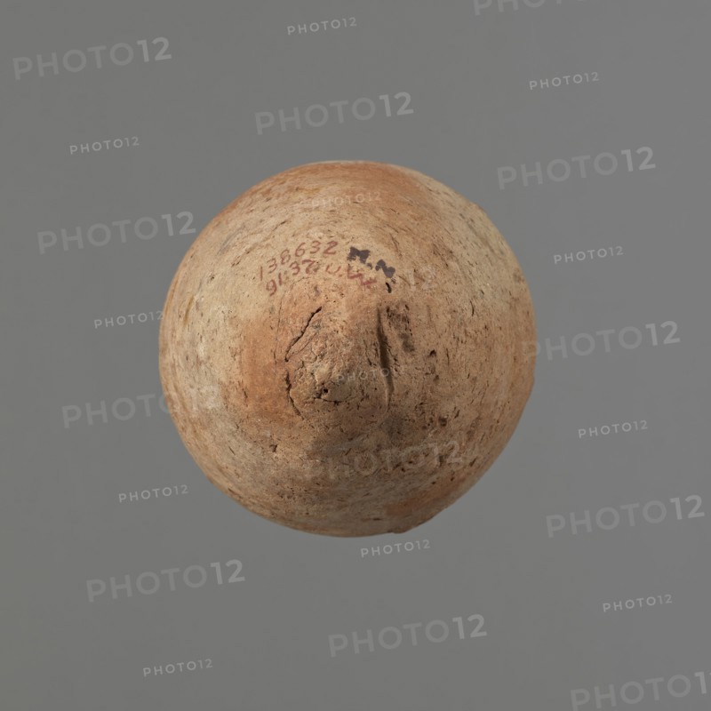Vessel with hieratic inscription. Egyptian pottery, clay conical vessel tapering toward the bottom, slightly irregular; widest at approx. 3/4 of the height. Narrow, slightly sloping shoulders; short, wide neck; thickened, rounded, slightly flaring rim; pointed bottom. Handcrafted, upper part shoulders, neck, rim turned. Smooth surface, externally probably covered with a layer of engobe. Made of Nile clay Vienna System. Color: red exterior, beige interior. Remains of a hieratic inscription in black on the lower part of the belly. Rim slightly damaged in several places. Old Kingdom, ca. 2686–2181 BC. Height 13.8 cm; rim diameter 5.9 cm; belly diameter 8.9 cm. Analogies: Petrie, Dendera; Hope, Akhmim; Reisner, Mycerinus; Brunton, Qau and Badari; Mace, Naga ed-Der; Reisner, Naga ed-Der; Petrie, Abydos; Keiser, Avila, Dreyer, Jaritz, Laskowska-Kusztal, MDAIK 40., A roughly spherical object with an uneven, textured surface sits against a plain gray background; the object shows a range of ear...