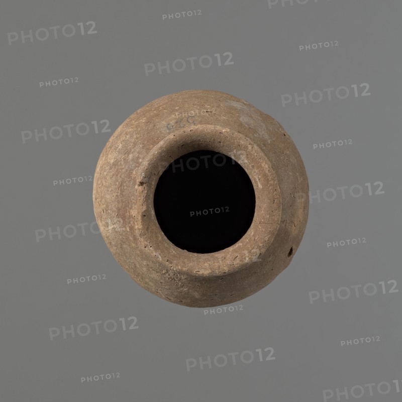 Vessel with hieratic inscription, Egyptian pottery, conical clay vessel tapering toward the bottom, irregular, widest at approximately 3/4 of the height. Narrow, sloping shoulders; short, wide neck; gently rounded, slightly flaring rim; pointed bottom. Handcrafted; upper part shoulders, neck, rim turned. Smooth surface, externally probably covered with a layer of engobe. Made of Nile clay NB2 Vienna System. Remains of a hieratic inscription in black on the lower part of the belly. Fairly well preserved; damage to the rim. Old Kingdom, Edfu. Height 14.6 cm; rim diameter 5.8 cm; belly diameter 8.7 cm. Analogies/citations: Petrie, Dendera; Hope, Akhmim; Reisner, Mycerinus; Brunton, Qau and Badari; Mace, Naga ed-Der II; Reisner, Naga ed-Der III; Petrie, Abydos II; Keiser et al., MDAIK 40; dated ca. 2686–2181 BC., A round, weathered clay vessel viewed from above with a wide circular opening showing a deep black interior, the exterior surface textured and pitted with an earthy brown color an...