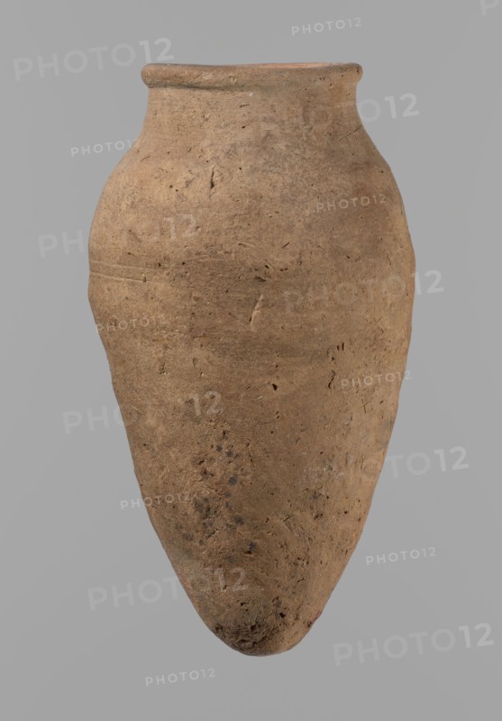 Vessel with hieratic inscription, Egyptian pottery ceramic clay vessel, Old Kingdom, ca. 2686–ca. 2181 BC, Edfu find site. Comparative material: Petrie, Dendera, pl. XVI,2; Hope, Akhmim, fig. 7, type AIVa 2bi; Reisner, Mycerinus, p. 212, fig. 64 3,4; Brunton, Qau and Badari, pl. LXXXI type 77N — earlier dated to the IVth–Vth Dynasty; Mace, Naga ed-Der II, figs. 87.11–14, 16–25; Reisner, Naga ed-Der III, fig. 28–33; Petrie, Abydos II, pl. XLIII, 79–80; Keiser, Avila, Dreyer, Jaritz, Laskowaska-Kusztal, MDAIK 40, fig. 9b. Vessel height 15.1 cm; rim diameter 5.6 cm; body diameter 8.2 cm., A large, rounded clay vessel with a narrow neck and flared rim suspended against a plain background; the surface shows a rough, textured appearance with small pits and irregularities and mottled coloration in shades of brown and tan with darker brown spots and flecks, and subtle variations of lighter beige in places.