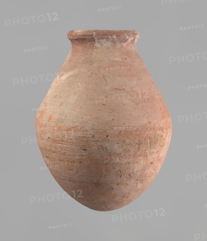 Vessel with an ovoid belly, a wide short neck and a rounded bottom. Straight, upturned rim. Wheel-made from Nile clay of type NB2 Vienna System. Surface levelled and outer surface covered with engobe. Outer surface red, inner surface yellowish-brown. Firing hole at the widest circumference approx. 1 cm diameter. Well-preserved. ca. 1550–1295 BC; New Kingdom, 18th Dynasty. From Deir el-Medina. Vessel; height 27 cm, rim diameter 11 cm, body diameter 20.5 cm., A large rounded clay vessel with a narrow flared neck and a slightly flattened rim, showing a rough, textured surface with visible tool marks and small pits; the vessel displays a range of earthy colors including terracotta, pale orange, light brown, and spots of beige, with subtle variations and patches of lighter and darker tones across its curved body, set against a smooth neutral gray background.