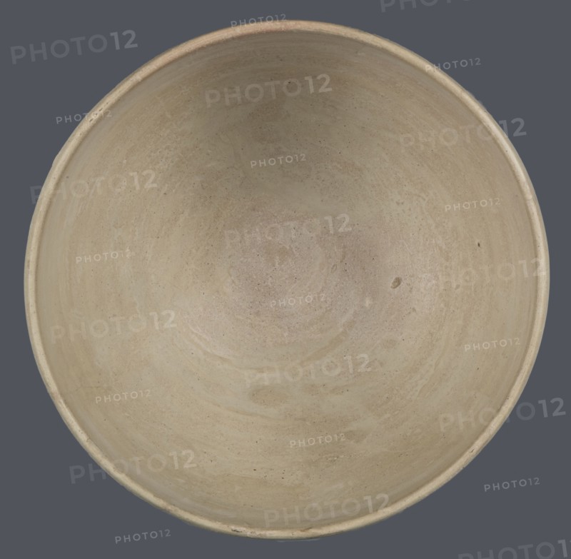 Bowl, unknown Northern Mesopotamian workshop; clay; Early Jazira III period ca. 2600–ca. 2350 BC / Early Dynastic III period; tableware vessel. Bowl with a flat, slightly oblique, oval bottom with traces of being cut off with a string, gently tilted walls that straighten and bend slightly inwards in the upper part, and a straight, undifferentiated rim. Northern Mesopotamia Khabur basin, Tell Rad Shakra Northeastern Syria., A top-down view of a round, shallow bowl with a smooth interior surface showing subtle circular marks and variations in texture, in beige and light tan tones with small darker speckles; the bowl sits against a flat, dark gray background.