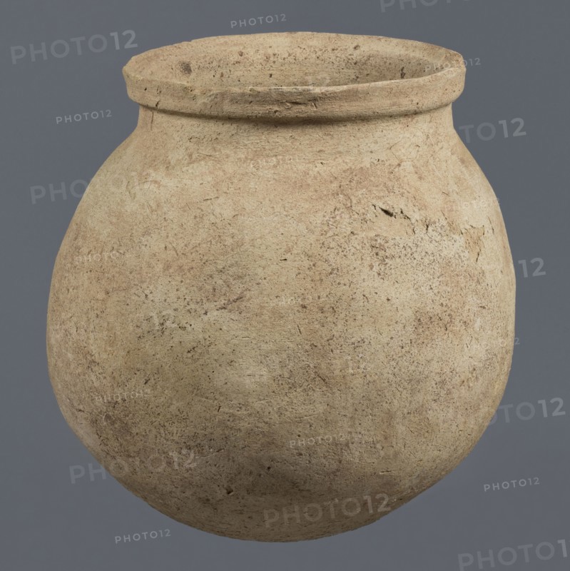 Spherical vessel, unknown northern Mesopotamian workshop, Early Jazira III period ca. 2600–ca. 2350 BC / Early Dynastic III period. A spherical vessel with a pear-shaped, tapering body with a rounded bottom, strongly sloping shoulders passing into a low, wide neck ending with a thickened rim on the outside in the form of a wide rectangular strip; the rounded outer edge of the rim protrudes above the inner surface of the neck, creating a lowered step for a lid. On the lower part of the body a pottery mark was carved before firing: two long lines intersecting at the bottom at an acute angle, forming a mark resembling a deformed letter Y. Material: clay. Origin: Northern Mesopotamia Al-Jazira/Khabur basin, Tell Rad Shakra northeastern Syria. Vessel; height 25.5 cm, width 24.6 cm., A large rounded clay vessel with a wide mouth and a thick rim, showing a rough, textured surface with small pits and irregularities, colored in shades of beige and light brown with darker brown speckles and patc...