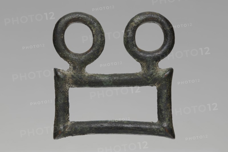 Buckle, Bronze buckle consisting of two parts in a shape similar to rectangles with joints. One part has hooks in the form of zoomorphic decoration animal heads. 7th century BC, Etruria. Decoration. Length 13 cm total; height 7.5 cm; thickness 4 cm; weight 0.374 kg; length 7.2 cm single element., A weathered metal object with a rectangular open center and a horizontal bar across the top, topped by a pair of circular loops; the surface shows rough, pitted texture and corrosion with visible patches of green, dark brown, gray, and black.