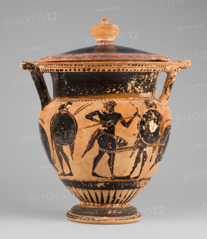 Column krater with lid, unknown Attic workshop. Black-figure krater with lid. Red clay, tinted with ochre; black firnis with a muted lustre, fading to brown in places. Rim decorated with a radial ornament and a schematic ivy sprig; shoulders with a series of vertical lines. Belly decorated with figural scenes. Side A: Dionysus with a cornucopia accompanied by a satyr and a maenad. Side B: an archer flanked by two helmeted hoplites with round shields. Lid with a pomegranate-shaped handle, decorated with an ivy sprig on the rim. Circa 520–510 BC, Attica. Vessel type: column krater. Weight 1.382 kg; diameters 19.2 cm body and 22.5 cm with vices; heights 21.4 cm body and 22.6 cm with vices., An orange terracotta vessel with a lid and two handles sits against a neutral gray background; the vessel shows black painted figures and decorative bands, with visible wear and flaking revealing the base orange color beneath; a group of black-figure human silhouettes and shields encircles the body, ea...
