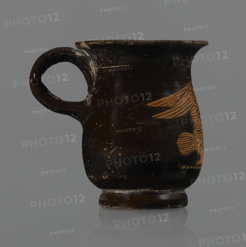 Jug, red-figure pottery, Greek, mermaid mythological, Athens Attica, 3rd quarter of the 5th century BC. A small jug with a low foot recessed at the bottom; edges of the foot slightly rounded and tapered upwards. Body slightly wider than the foot, rounded at the bottom, almost cylindrical in the lower half and gently tapering in the upper half, merging into a widely flared outward spout. Below the spout is a vertically mounted, cylindrical, slightly flattened handle bent into a circle. Light orange clay with black shiny varnish. On the body a mermaid in right profile with wings raised upwards left wing behind, protruding above the right; on her head a diadem marked with white dots. Feathers indicated by lines—long and thin at wingtips and tail; thin and thick elsewhere. Image emphasized below with a row of dots. Side of the foot chipped, rim edge slightly chipped, varnish abrasion; part of the rim filled with plaster. Vessel height 6.6 cm., A dark brown ceramic cup with a rounded body, ...