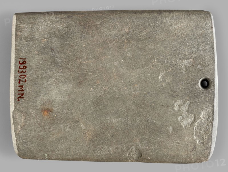 Rectangular paddle, flat with a hole at one of the shorter edges; possibly a whetstone. Ceremonial/toiletry geometric paddle, Predynastic Period Naqada III, 2nd half of the 4th millennium BC, Egypt. Height 8.2 cm, width 11.1 cm, weight 0.174 kg., inscription/author entries unspecified; provenance: Frombork Warmian-Masurian Voivodeship., A rectangular flat stone slab with rounded corners and a small circular hole near one short edge, showing a rough, scratched surface texture with patches of smoother wear and a few small areas of flaking; the visible colors are gray, light gray, brownish-gray, a few rusty brown spots, and a tiny hint of green.