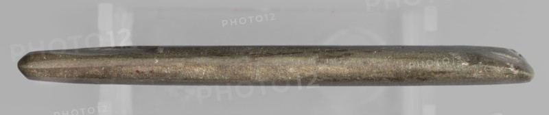Rectangular paddle with a hole at one of the shorter edges; possibly a whetstone. Flat rectangular paddle, geometric design. Predynastic Period Naqada III phase, 2nd half of the 4th millennium BC, Egypt. Paddle; height 8.2 cm, width 11.1 cm, weight 0.174 kg., A long narrow metallic object is shown horizontally against a light gray background, with rounded tapered ends and a slightly irregular surface texture; the object displays a mix of dull metallic colors including shades of gray, bronze, and brown with small lighter flecks and subtle darker streaks along its length.