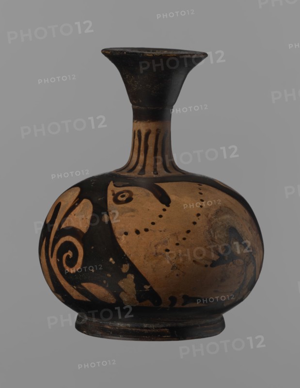 Aryballus lekythos, Ancient Greece, antiquity. Bird iconography. Ceramics; red-figure pottery; Greek pottery; ancient vessel; lekythos; Southern Italy. Reddish-brown clay with black, slightly shiny, well-covering varnish, also on the underside of the foot and inside the handles. Low echinus-shaped foot; spherical, slightly flattened body. Low, narrow neck with a funnel-shaped rim with a thickened lip. Body decoration: bird in left profile with beak raised. 4th century BC. Aryballus lekythos vessel. Height 9.3 cm; width 7.6 cm., A rounded ceramic vessel with a narrow flared neck sits against a plain gray background, showing a palette of black and tan with areas of lighter brown wear; the neck is primarily black with vertical tan stripes, the bulbous body features sweeping black painted motifs and dotted patterns on a tan field, and the base is dark with signs of surface aging and small patches where the black paint has worn away.