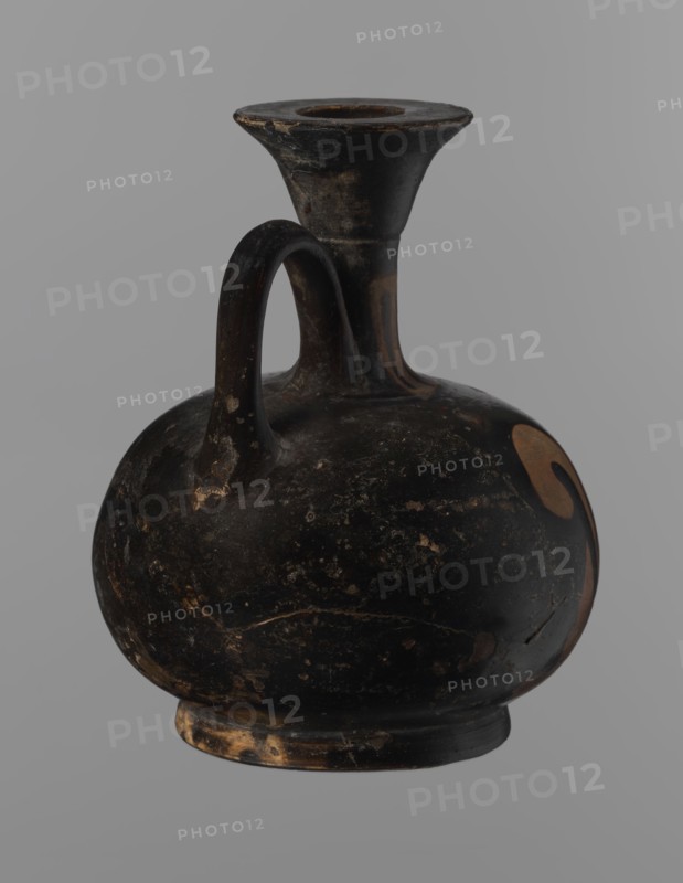 Aryballus lekythos, Reddish-brown clay with black, slightly shiny, well-covering varnish, including underside of foot and inside handles. Low echinus-shaped foot, spherical slightly flattened body; low narrow neck with funnel-shaped rim with thickened lip. Body decorated with a bird in left profile with beak raised. Ceramics, red-figure pottery; Greek pottery, ancient vessel lekythos / aryballus. Southern Italy, 4th century BC. Height 9.3 cm, width 7.6 cm., A rounded, bulbous ceramic vessel with a single curved handle connecting the body to a tall, flared neck and rim; the surface shows worn, chipped areas and a mottled texture. The vessel is predominantly black with patches of brown and tan where the surface has worn away, and there is a small area of lighter brown on one side of the body. The rim and base show visible wear with exposed tan and brown tones, and the handle has small worn spots revealing lighter brown beneath the black. The background is a uniform gray.