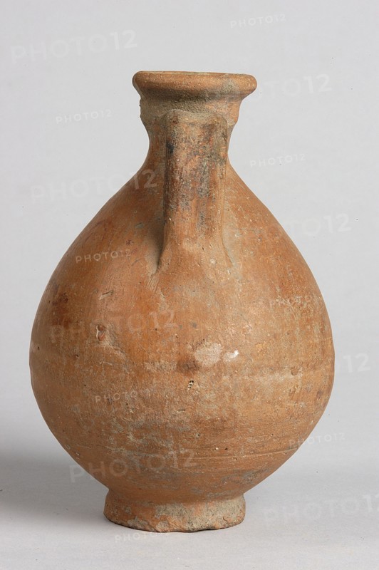 Pelike; decoration painted on the firnis: between the handles on both sides, a wavy linear tendril with volute-like curled side shoots. Above it, a wavy line twist?. At the height of the base of the handles, two horizontal parallel lines. 332–30 BC; Hellenistic period., Vessel; height 12.5 cm, width 9.8 cm., A rounded, bulbous clay vessel with a narrow neck and a short flared rim, featuring a single vertical handle running from the rim to the shoulder; the surface is textured and worn with patches of roughness and small pits, showing shades of terracotta, brown, and muted grayish areas, set against a plain light gray background.