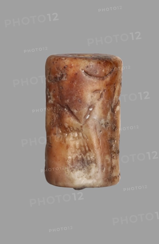 Cylinder seal with a presentation scene and a cuneiform inscription, unknown Akkadian workshop; maker: Mardati scribe. Cylinder with a negatively engraved presentation scene showing three male figures, one seated and two standing before him. Behind the seated figure are two vertical frames with cuneiform characters. The seated figure on a damaged throne is in left profile, wearing a kaunakes-type robe and a headdress with a single pair of horns typical of deities; the right hand is raised in a gesture of greeting toward the approaching figures. In front of him is an altar or censer, and in the upper register is a crescent moon. Behind the altar stands a figure in right profile wearing a long robe with fringes; the left arm is bent and raised to face level in greeting, the right arm bent at the elbow is at waist level. Behind the deity, a standing figure in right profile wears a long robe with fringed hem; his lowered left hand holds a bucket or basket, and his right hand, bent at the e...