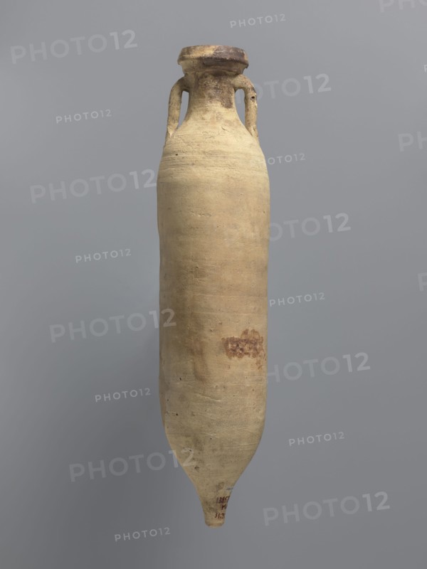 Amphora spatheion, unknown North African workshop Tunisia/Libya. Cylindrical, elongated amphora with a smooth yellow-green surface, probably covered with a coating produced during the firing process natural engobe, self-slip. Two-stage profiled spout with a rounded top and an outward-sloping lip. Small loop-shaped handles attached to the shoulders and to the neck just below the spout; conical bottom. Inner walls covered with a resin impregnation, which is also visible on the outer walls of the upper part of the amphora. Complete vessel; ceramic body not visible. 2nd half of the 6th–7th century. Found at Edfu. Vessel amphora. Height 44.2 cm; rim diameter 6.6 cm; body diameter 10 cm., A tall, elongated ceramic vessel with a narrow, pointed base and a wider rounded body tapering to a short neck with a flared rim, featuring two small loop handles near the neck; the surface appears textured and worn with an overall beige or light tan color, areas of darker brown and reddish-brown discolorat...