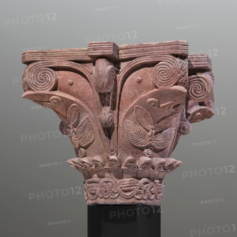 Upper and lower fragments of the capital reconstructed to their complete form. Nubian workshop. Architectural element; capital preserved in two fragments, reconstructed to its complete form. The high neck is decorated with a wavy vine twig with stylized leaves at the bottom and clusters at the top in an alternating arrangement. Above the neck, the shaft is decorated with a wreath of small plastic leaves adorned with small loops of ribbon. The shaft is decorated with large, wide, smooth leaves. On their surface, branches with symmetrically arranged leaves and marked veins are depicted in relief. Between the wide leaves are ribbons arranged in a V-shape, forming volutes at the top. Decorative, plastic elements in an S-shape emerge from between the ribbons, forming supports for the abacus's protrusions. The abacus is low, divided into three layers by two engraved lines. Large capitals of this type were part of the decor of the older basilica and topped the columns of the main nave; pairs ...