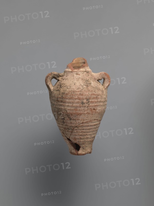 Water vessel qulla, bottle gulla. Ovoid, elongated body, wider in upper part, above half the vessel's height. Low foot, hollow inside, poorly defined externally. Two small vises are glued to the arms, and between them, on an axis perpendicular to their attachment, a conical spout for drinking water is glued. The neck, preserved in its lowest part, is separated from the body by a small, sharply profiled hump. The entire surface of the vessel is covered with light whitewash. Nile clay, medium-porous, 5th century, Tell Atrib, vessel; height 17.0 cm, width 11.5 cm, diameter 4 cm base., An aged clay vessel with a rounded body tapering to a narrow base and a broken tip, featuring a pair of loop handles near the shoulder and horizontal ridged bands around the lower half; the surface shows rough texture, chips, and cracks with areas of wear. The visible colors are muted beige, terracotta, pale brown, and some darker grayish spots against a neutral gray background.