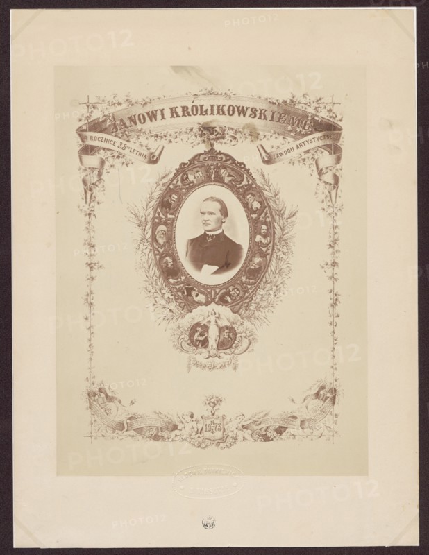 To Jan Królikowski on the 35th anniversary of his artistic profession. 14/4 1873, Kloch, Ferdynand i Dutkiewicz, Melecjusz photographic studio; 1866–1874 authors, Gerson, Wojciech 1831–1901 draughtsman; co-author, Królikowski, Jan Walery 1820–1886, male portraits; iconography of Jan Walery Królikowski; portraits; actors; theatre artist; anniversaries; photographic tableau; theatre costumes; print glued with the entire surface onto cardboard; 1873; Warsaw; photography; photographic tableau; reproduction of a work of art; photographic print: 25.1 × 19.0 cm; cardboard: 32.9 × 24.7 cm, A sepia-toned ornamental print featuring a central oval portrait of a man wearing a dark jacket and white shirt, set within an elaborate decorative frame with floral wreaths and small portrait medallions; above the oval is a curved ornamental banner and scrolling foliage, and below it is an ornate cartouche with decorative figures and flourishes; the composition is bordered by vertical floral garlands on bot...