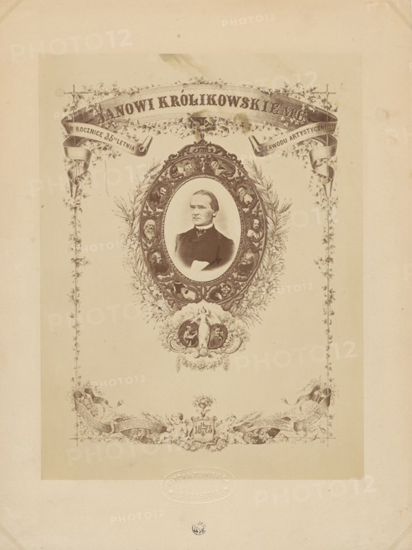 To Jan Królikowski on the 35th anniversary of his artistic profession. 14/4 1873, Kloch, Ferdynand i Dutkiewicz, Melecjusz photographic studio ; 1866-1874 author, Gerson, Wojciech 1831-1901 draughtsman co-author, Królikowski, Jan Walery 1820-1886, male portraits, Królikowski, Jan Walery 1820-1886 - iconography, portraits, actors, theatre artist, anniversaries, photographic tableau, theatre costumes, print glued with the entire surface onto cardboard, 1873, Warsaw, photography, photographic tableau, reproduction of a work of art, photographic print: height 25.1 cm, width 19.0 cm; cardboard: height 32.9 cm, width 24.7 cm, A sepia-toned ornate portrait sheet with a central oval frame containing a photographic bust of a man wearing a dark suit and a high collar, surrounded by an intricately decorated wreath-like border with small portrait medallions and floral motifs; decorative ribbon banners and vine-like embellishments extend along the top and sides, and a decorative cartouche with clas...