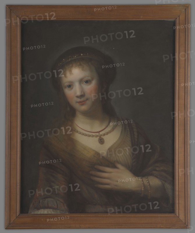 Saskia von Uylenburgh 1612–1642, wife of Rembrandt; copy after Rembrandt van Rijn 1606–1669. Half-length, full face portrait, after 1641. Light hair falling on the shoulders and forehead; wearing a beret decorated with stones, a golden dress with a large neckline and a shawl over her shoulders. Around her neck: a string of pearls and a medallion with a blue stone on a chain. Her left arm, bent at the elbow, is decorated with two golden bracelets that support the coat on the chest. Background dark and plain. This is a fragment from Rembrandt’s painting Saskia with a Red Flower; in this portrait the flower is not visible, only the outstretched arm. Portrait, height 64.5 cm, width 54 cm., A framed portrait of a person shown from the waist up wearing a dark head covering and a layered outfit with a shawl; the background is dark gray to black, the frame is brown wood, the person has light skin with pinkish cheeks, light brown hair, and blue-gray eyes, and they wear a few necklaces and a pen...
