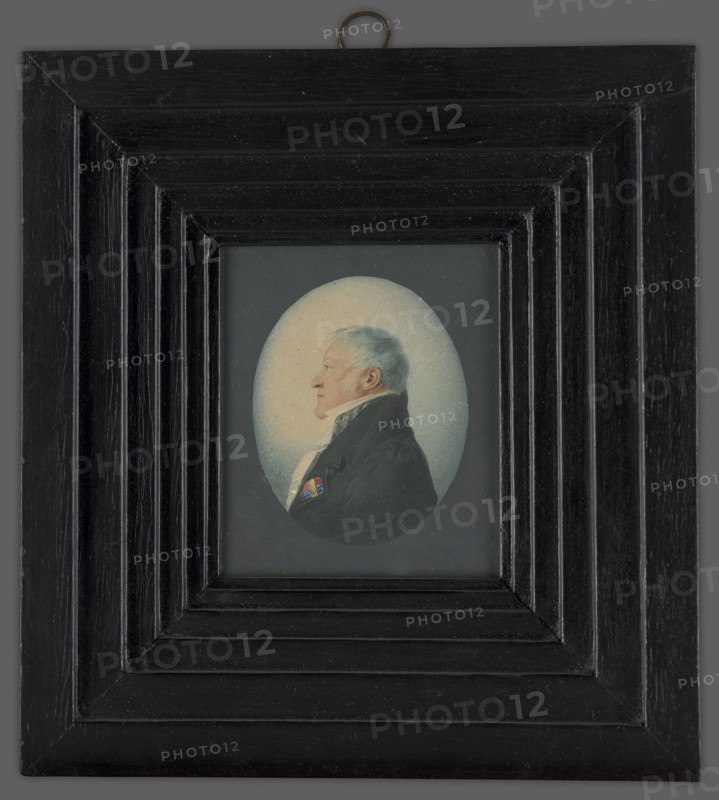 Karol Otto Kniaziewicz 1762–1842, unknown author. Bust of a man in left profile. Blue eye, grey-blond hair. A white shirt with a high collar, a light-striped vest, and a black tailcoat with a red, blue, and gold ribbon pinned to the left lapel. Blue background. Depicted in civilian attire with the berets of the Legion of Honor and the Virtuti Militari Cross, fastened with a gold plaque with diamond stars. Two similar miniatures: one of General Stanislaw Fiszer and one of Lieutenant Colonel Ignacy Hauschild, circa 1810. A copy of the miniature was made in 1815 by Aleksandra Radziwillowa née Stecka, the general's stepdaughter, in the album of Ludwika Antoniowa Radziwill, after 1815, Poland. Type: miniature., A framed oval portrait of an older man in profile, set within a rectangular multi-stepped black wooden frame with visible wood grain and a small metal hanging loop at the top; the man has light gray hair and pale skin, wears a dark coat with a high collar and a white cravat, and a sm...